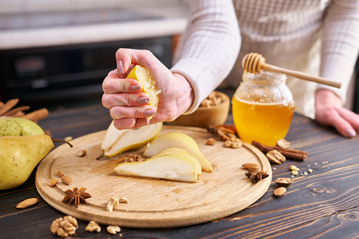 Woman squeezeing fresh lemon juice onto Ripe organic pear on the wooden cutting board Board at domestic kitchen.