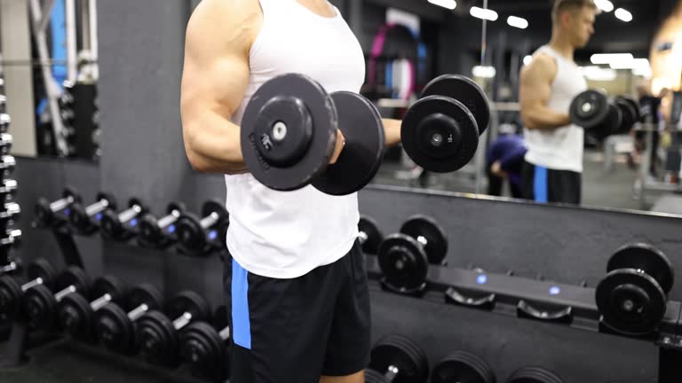 Bodybuilder doing biceps-triceps workout with dumbbells in gym