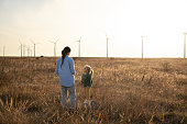 Mom and kid in wind farm at sunset in autumn. Sustainable future concept. copy space