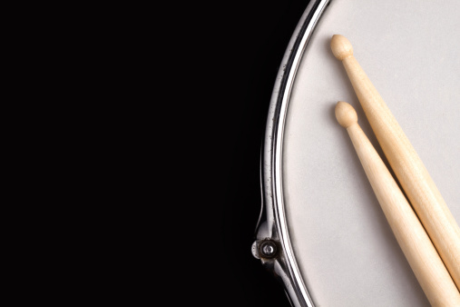 Snaredrum with coated head and drumstick on black background with big copy space for text.