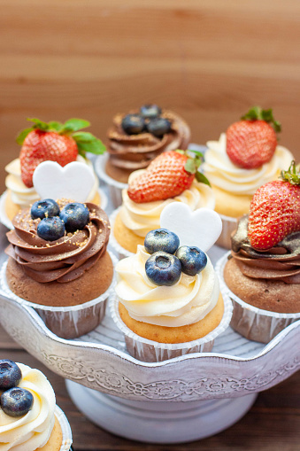 Chocolate and vanilla cupcakes with blueberries and fresh strawberry on a marble cake stand