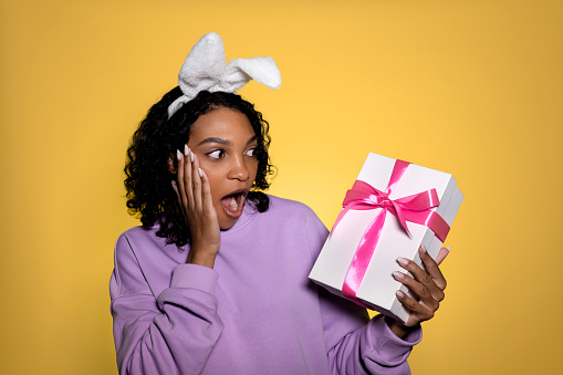 Easter concept. Funny surprised african american woman looking at the gift box. Exclusive offer,discount and sales concept