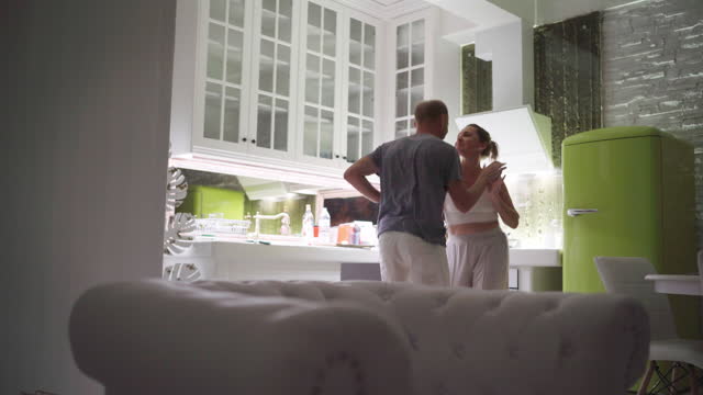 Funny middle aged couple man and woman graceful amusingly dancing in cozy home kitchen.  Enjoying life concept 4K video.