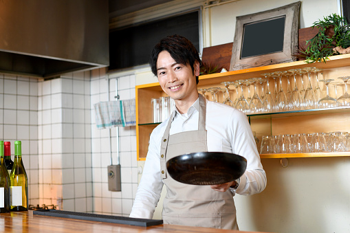 Asian man looking at camera cooking with frying pan in restaurant kitchen