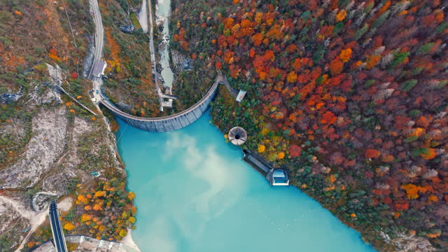 AERIAL Drone Directly Below Shot of Dam and Calm Turquoise Lake Amidst Autumn Trees in Italy
