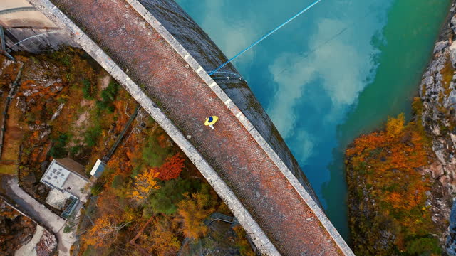 AERIAL Drone Directly Above Shot of Male Tourist Walking on Concrete Arch Dam in Italy