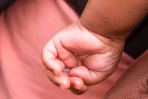 Description: Macro image of an infant's hand grasping the parent's thump. White Background.