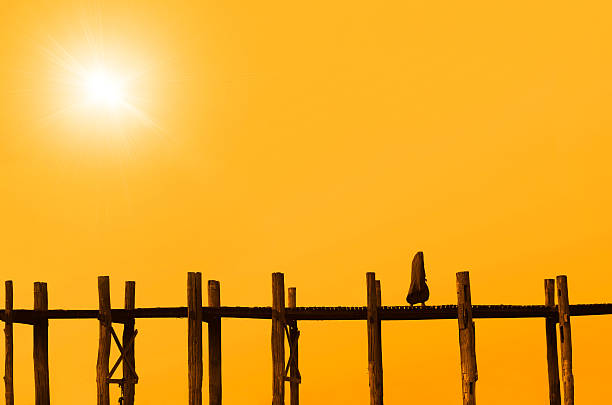 Silhouette crossing woden bridge at sunset Silhouette of a Buddhist monk crossing Ubien, the longest teakwood bridge on the world mickey mantle stock pictures, royalty-free photos & images