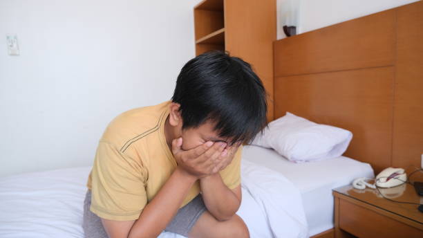 顔を覆いながらベッドの脇に座りながら後悔する東南アジア人男性 - hangover men crying bed ストックフォトと画像