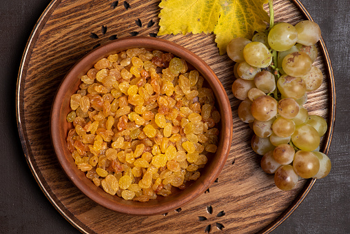 Fresh white grapes on a wooden tray and dried white grapes or raisins in a bowl. View from above