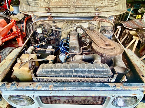 Horizontal still life of rustic + rusted old ute truck's bonnet hood with engine and parts parked in farm shed on rural country property Australia