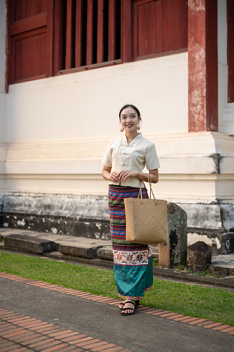 A portrait of a charming young Thai-Asian woman in a traditional Thai-Northern dress is in a beautiful temple. Thai culture, Buddhism, cultural travel, and lifestyle, full body picture