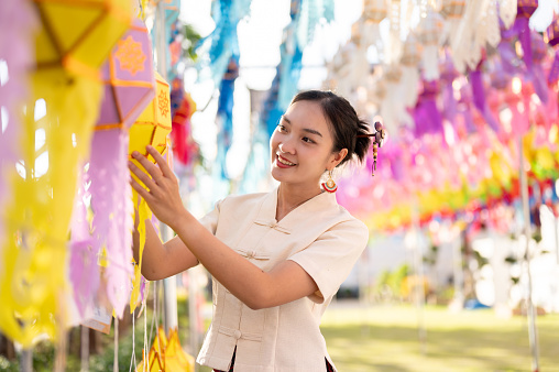 A beautiful and happy Thai-Asian woman in traditional dress is hanging a paper lantern and enjoying YI Peng or Loy Krathong festival at a temple in Chiang mai. Thai-Lanna culture, Thai festival