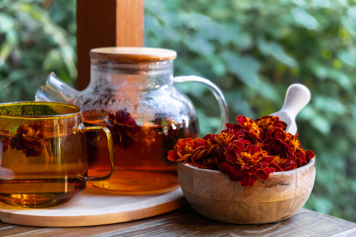 Marigold tea still life on table in green garden background. Healthy hot drink benefits. Natural organic aromatic drink in cup. Home-grown immunity-boosting herbs for tea. Autumn winter warming drink