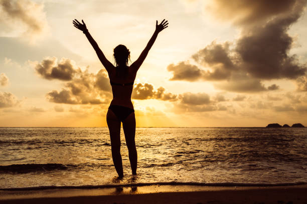istock Woman's silhouette with raised arms against calm sunset beach 1794178641