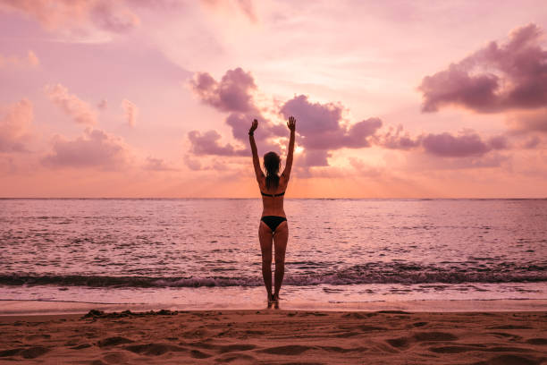 Woman's silhouette with raised arms against calm sunset beach