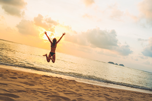 Silhouette of happy joyful woman jumping and having fun at the beach against the sunset. Freedom and vacation concept
