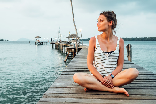 Young woman meditating on pier in lotus position at sunrise