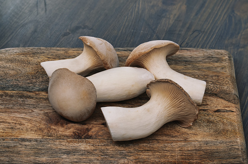 Fresh king oyster mushrooms, vary in sizes, rest on a wooden cutting board, background grey-blue toned wooden surface, vibrant scene of food preparation