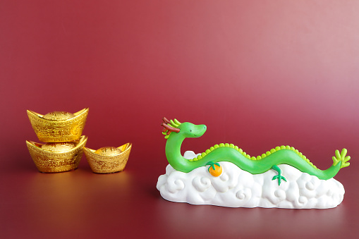 The green dragon statue and gold sycee on red background. 2024 New Year.Chinese new year decoration with copy space