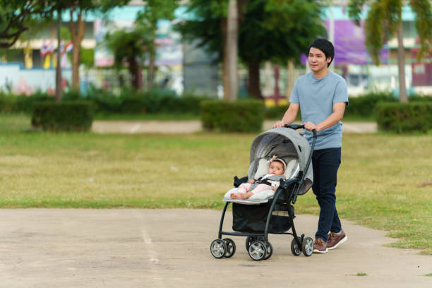 happy father pushing infant baby stroller and walking in park