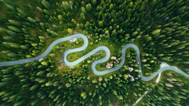 Aerial view Real time Footage of car driving on the snake-like curvy road or sneak road Surrounded by pine trees in Dolomites, one of the most famous in the Dolomites Alps, Italy