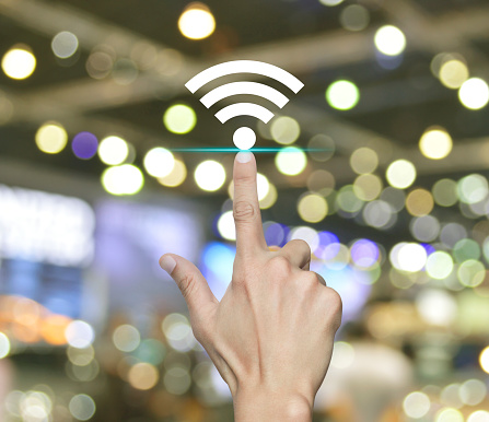 Hand pressing wi-fi flat icon over blur light and shadow of shopping mall, Technology internet communication concept