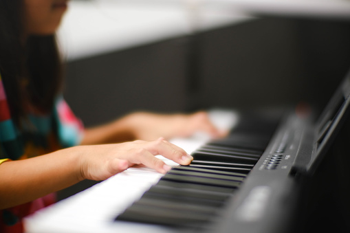 Close-up of a little student's hand playing the piano. Happy young Asian girl learning and practicing the piano. Selective focus.