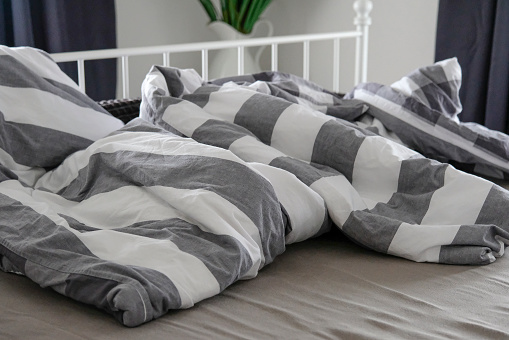 Morning shot of a rumpled double bed with striped bed linen.