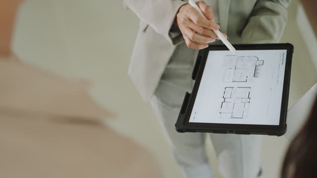 Close up of Real Estate Agent explaining floor plan house blueprint on a digital tablet to couple buying a property house