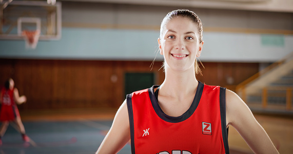 Portrait of smiling female basketball player standing on sports court during practice.