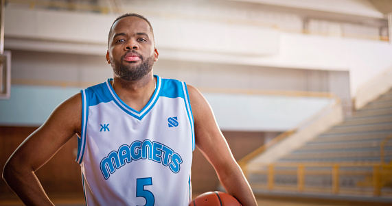 Portrait of male basketball player holding basketball while standing on sports court during practise.