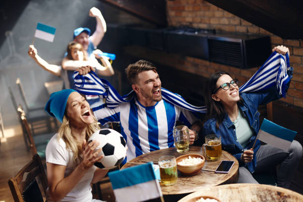 istock Cheerful fans cheering while watching a soccer match on TV in a bar. 1794378977