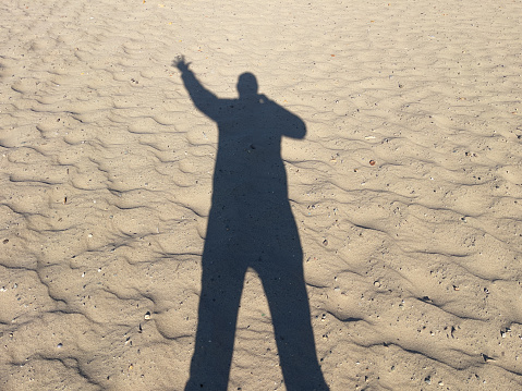 Silhouette of a man standing on the seashore with his hand raised. Greeting.
