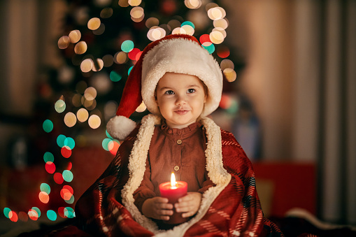 A cute little girl is sitting at home on christmas and new year's eve with candle in her hands.