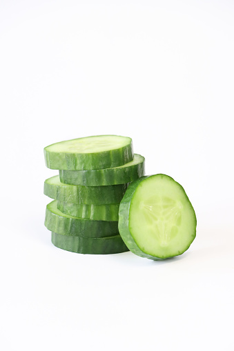 Stock photo showing close-up view of healthy eating image of a stack of sliced cucumber on white background. Pieces of cucumber (Cucumis sativus) displaying green skin and white flesh with white seeds.