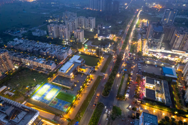 aerial drone shot showing brightly lit street with multi story sky scrapers offices, homes, shopping malls, sports arenas and more in metropolitan city like gurgaon, delhi, mumbai, bangalore stock photo