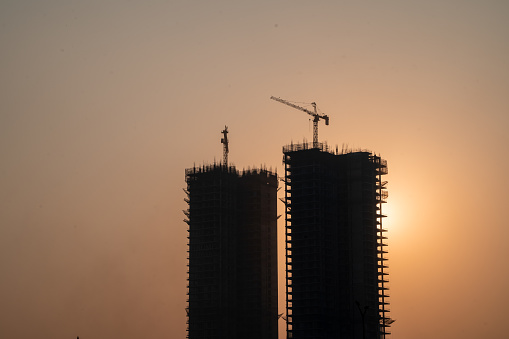 Silhouette of under construction building against sunset with crane on roof showing rapid real estate infrastructure growth in gurgaon delhi mumbai in India