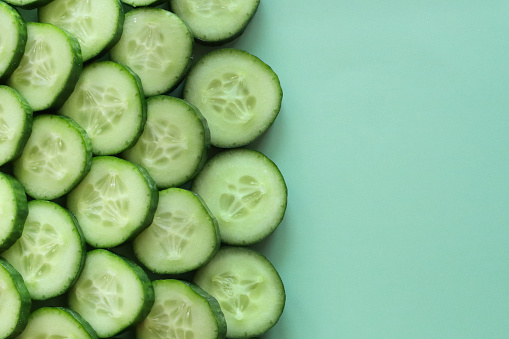 Stock photo showing close-up, elevated view of layers of cucumber slices. Overlapping pieces of cucumber (Cucumis sativus) displaying green skin and white flesh with white seeds, healthy eating poster wallpaper background design.