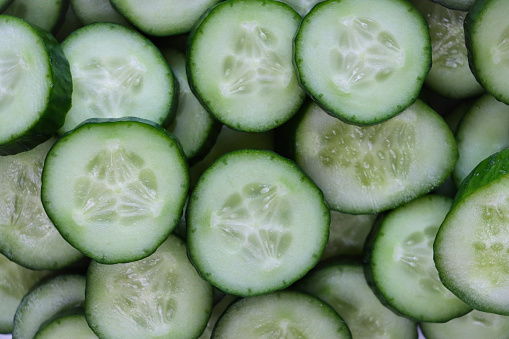 Stock photo showing close-up, elevated view of stacked layers of cucumber slices. Pieces of cucumber (Cucumis sativus) displaying green skin and white flesh with white seeds, healthy eating poster wallpaper background design.