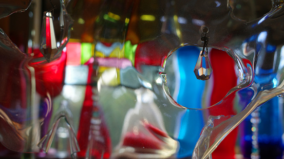 A curved piece of plexiglass with crystal drops in it. The background with glass bottles is distorted by the plastic.