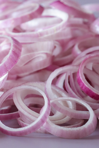 Stock photo showing a close-up view of healthy eating image of red onion rings. Pieces of vegetables displaying purple skin and white flesh on purple background.