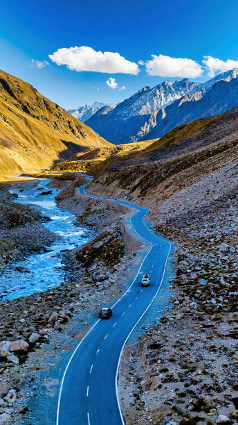 Aerial view of a road alongside river stream through mountains