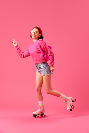 Full length portrait of young woman, model wearing fashion outfit with modern pink accessories have fun rollerblading isolated vivid studio background. Concept of youth, style, human emotions. ad
