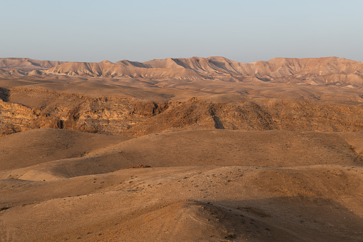 First light of sunrise casts a golden glow on the mountainous, dry, barren landscape of Israel's Judean Desert.