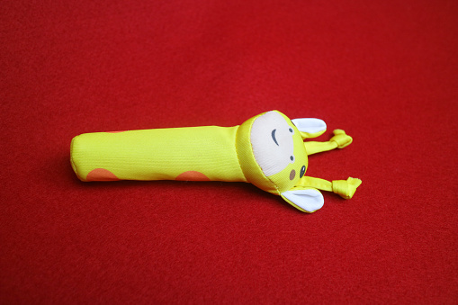 A yellow giraffe shaped baby holding toy that makes a sound when squeezed. on a red background