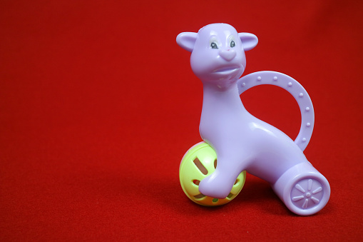 A toy shaped like an alpaca animal, purple in color, holding a ball. on a red background