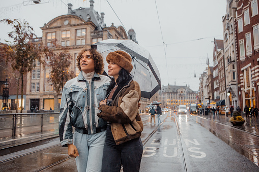 Romantic rainy day out in the Amsterdam streets for a diverse tourist couple made up of an alternative brunette female and a curly transgender woman