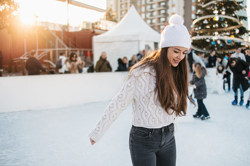 A young woman is skating on the ice rink, surrounded by blurred people. Winter and holiday activities