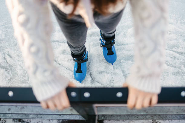 The ice skater is holding onto the railing to avoid falling. Sun during winter days